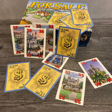 Load image into Gallery viewer, For Sale box with face up cards with houses and numbers on them as well as cards with money showing. All cards have braille stickers on them.
