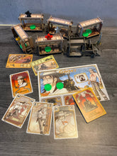 Load image into Gallery viewer, A shot showing the train cars. On the train car you can see the player pieces and the loot. In the foreground you can see the cards and a player mat. All of the pieces and cards have braille on them.