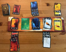 Load image into Gallery viewer, A picture of the game and the board laid out. Braille stickers are on all of the cards and the board. The board is two sided and the 5 expedition side is shown.
