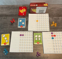 Load image into Gallery viewer, The game is shown setup(red version). There are trays next to the cards to sort who's dice are who's. The cards all have transparent braille on them indicated the needed dice and their point value