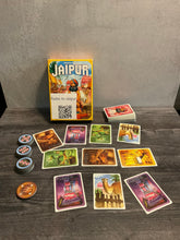 Load image into Gallery viewer, The game Jaipur laid out with a market in the middle between two players. The different favor tokens are shown to the left, with braille on both sides of the tokens