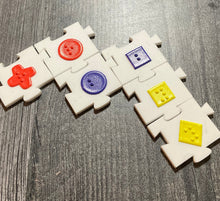 Load image into Gallery viewer, Close up on linked acrylic pieces. Tactile shapes are on all of the tiles and they fit together like jigsaw pieces. Braille is on the tactile shapes to tell the user the color.