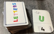 Load image into Gallery viewer, The Letters deck sitting next to a U flipped face up