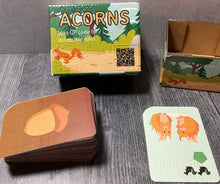 Load image into Gallery viewer, Picture of the Acorns box with the cards in front of it.