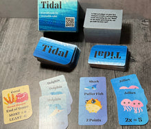 Load image into Gallery viewer, A picture of the Tidal box and some of the cards laid out in front. Coral, dolphins, Sharks, puffer fish and Jellies are shown.