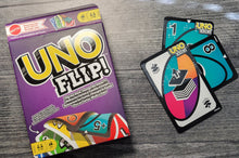 Load image into Gallery viewer, UNO Flip! game box and cards on a wooden surface. The cards have braille on them. The cards have braille on both sides but you can't see that.