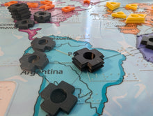 Load image into Gallery viewer, Black game pieces on a map of South America. The map has braille on it and tactile shapes denoting the border between South America and the other continents.