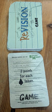 Load image into Gallery viewer, A close-up of the 'game' cards of revision on a wooden surface. One card is the back, featuring a light green background with blue lined notebook-style stripes and the word 'Revision' in red and blue. The card describes the way that players gain points this round.