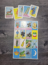 Load image into Gallery viewer, The Loteria board with some tokens on it and 5 call cards laid out above it.