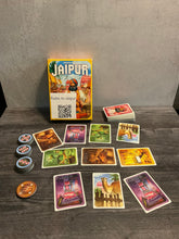 Load image into Gallery viewer, The game Jaipur laid out with a market in the middle between two players. The different favor tokens are shown to the left, with braille on both sides of the tokens
