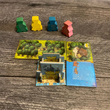 Load image into Gallery viewer, The meeples with braille on them. in front of them is the starting castle, and two domino tiles with forest and water. All are labeled in braille
