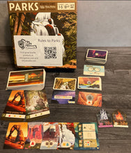 Load image into Gallery viewer, The parks game box with a bunch of types of cards and tokens set out that have been modified with transparent braille
