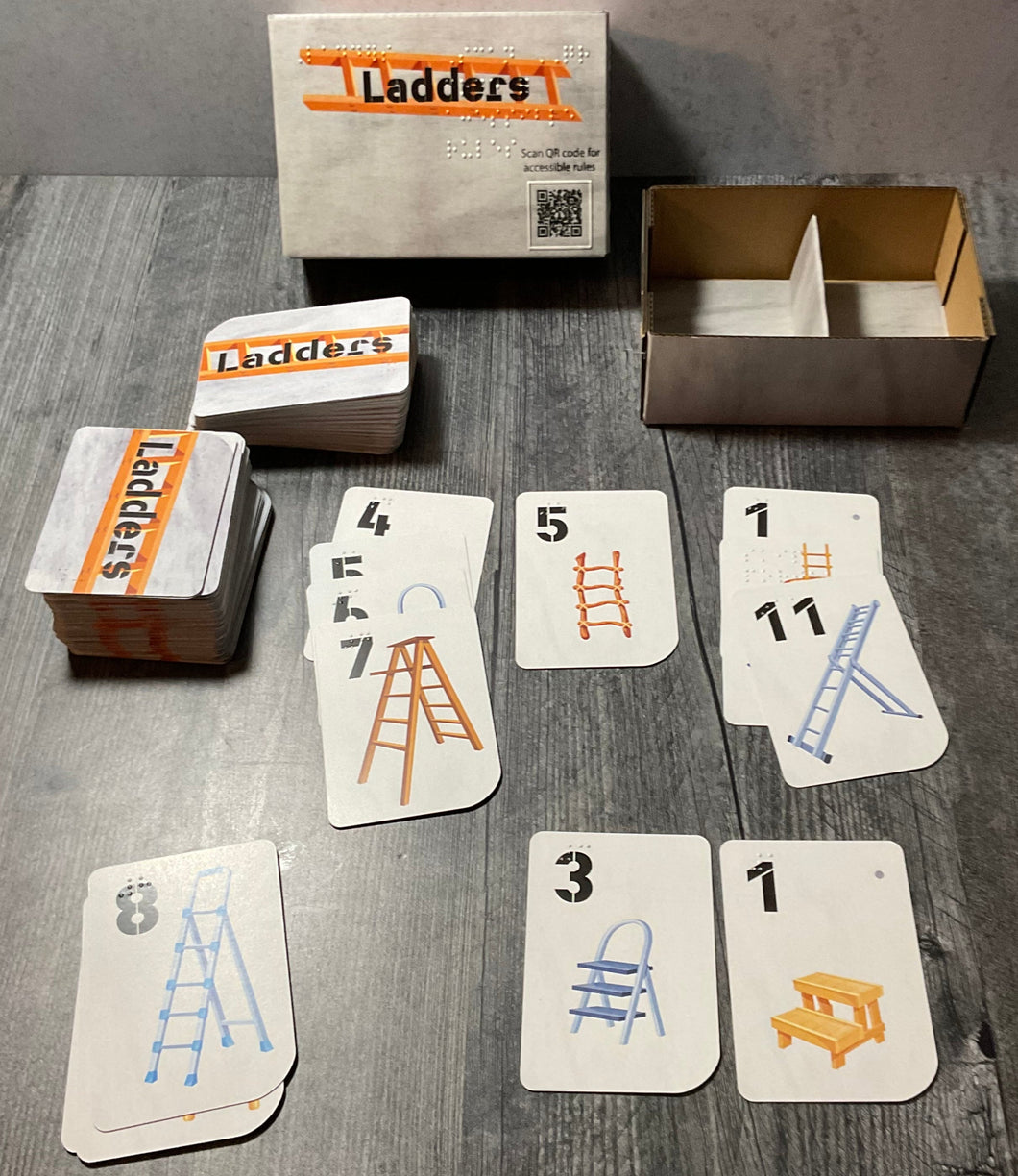 The ladders box laid out with a bunch of cards setup as they would be with gameplay. All the cards have print and braille and depict different ladders.