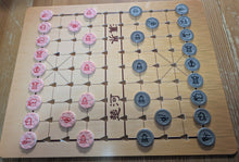 Load image into Gallery viewer, An acrylic Chinese chess board with a wooden print on a wooden table, featuring a light tan board with embossed grid lines, red and gray pieces with braille, and Chinese characters printed on the board.
