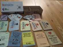 Load image into Gallery viewer, The box of Revision card, with the cards laid out in front and tokens displayed on a wooden tabletop. The custom playing cards, the rule change cards and round cardboard revision tokens.
All cards have both large print and Braille.
